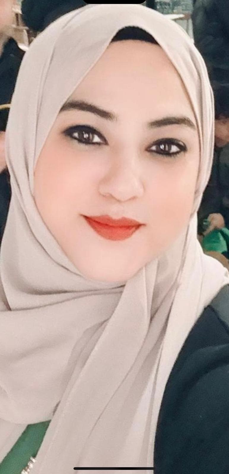 Close-up of a woman wearing a light beige hijab, dark eyeliner, and orange-red lipstick.