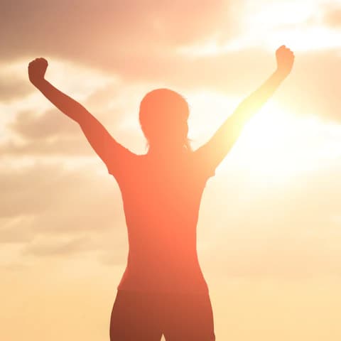 Silhouette of a person with arms raised triumphantly against a bright, glowing sunset sky.